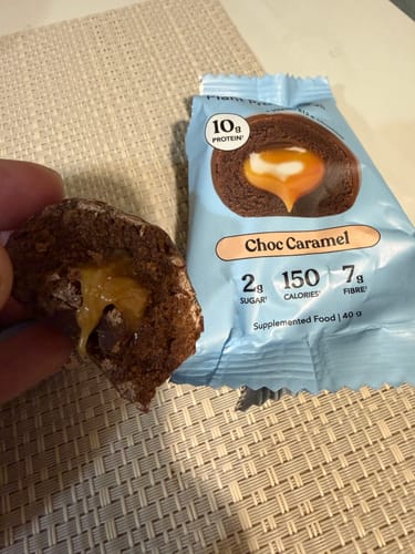 Customer holding a half-eaten Choc Caramel Plant Protein Ball, showing the gooey caramel filling inside.