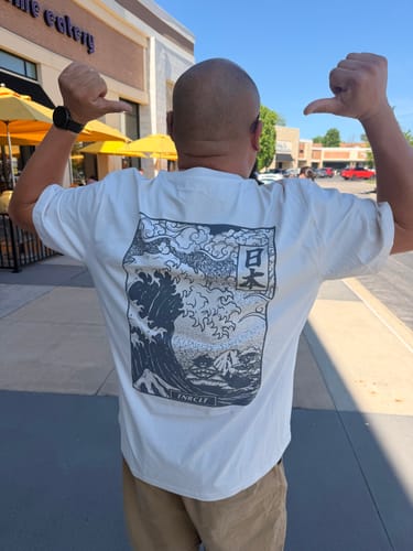 Customer seen from behind wearing the white VOLCANIC WAVES TEE, showing the back graphic.