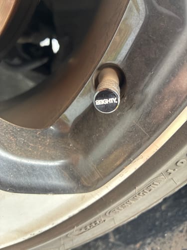 Close-up of a customer's black 80Eighty Valve Stem Cap installed on a car wheel.