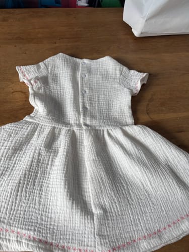 Customer's handmade dress from ivory double gauze fabric, showing the back with buttons and pink stitching on a table.