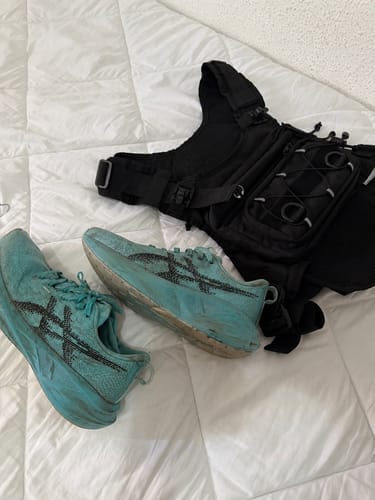 Sacca acqua portatile HydroRun di un recensore, posata su un letto accanto a un paio di scarpe da corsa.