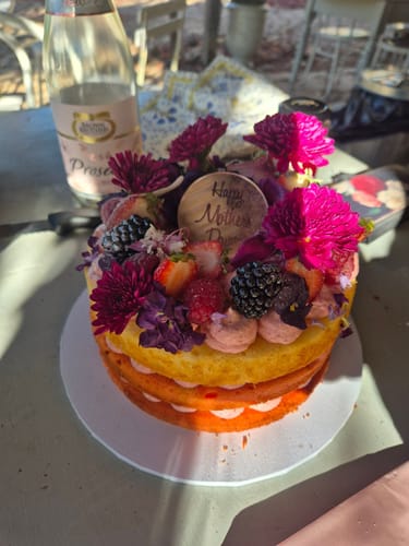 Reviewer's two-layer cake decorated with vibrant PURPLE PASSION FLOWERFETTI®, fresh fruit, and a Mother's Day sign.