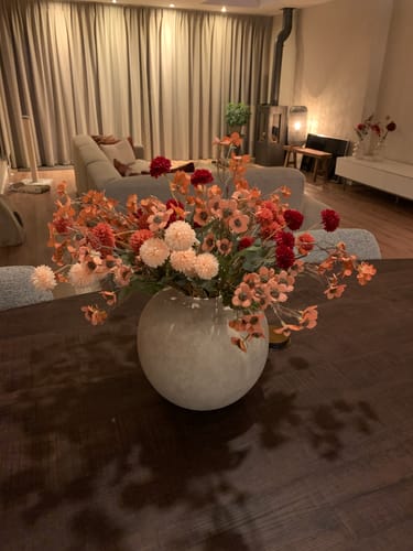 Klantfoto van het Wax Arrangement in een grote, ronde grijze pot, op een donkere houten tafel.