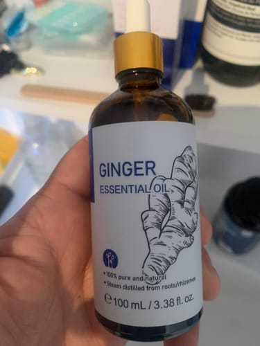 A customer holds the bottle of Ginger Essential Oil, showing its label with a large ginger root illustration.