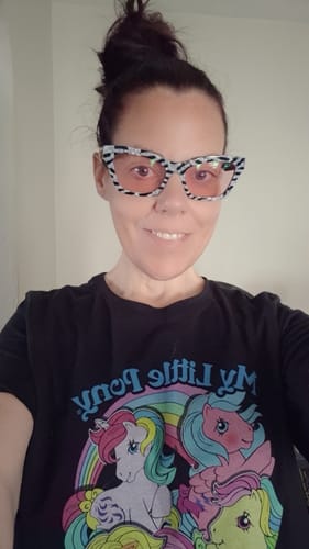 Reviewer smiling while wearing her black Womens Rainbow Collage My Little Pony Shirt.