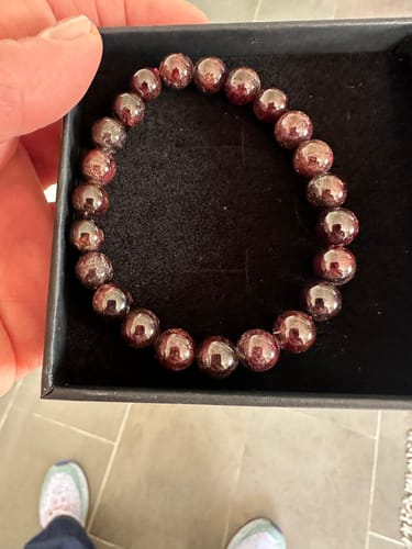 Client tenant le Bracelet Grenat avec des perles rouge foncé dans sa boîte noire.