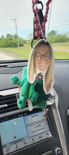 A customer's custom air freshener, featuring a photo of a person's face, hanging inside a car.