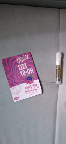 Customer shows their Grape Soda 10-OH HHC Superior Live Resin Cartridge and its packaging on a gray sofa.