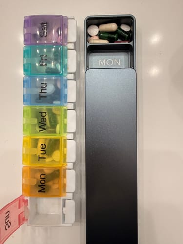 Reviewer's sleek metal Weekly Case shown next to a colorful plastic pill organizer.