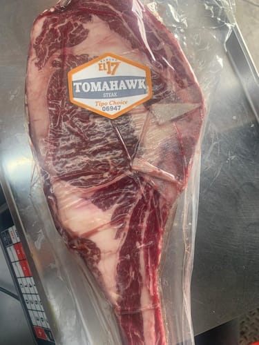 Cliente muestra un filete Rib Eye Tomahawk envasado al vacío, con veteado visible.