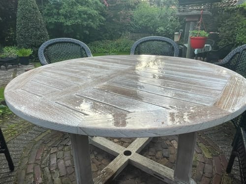 Recensent's ronde houten tuintafel in een tuin. Het natte oppervlak reflecteert na behandeling met Teakhout Care 202.