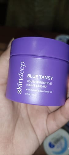 Reviewer holding the purple jar of BLUE TANSY Youth Preserve Night Cream.