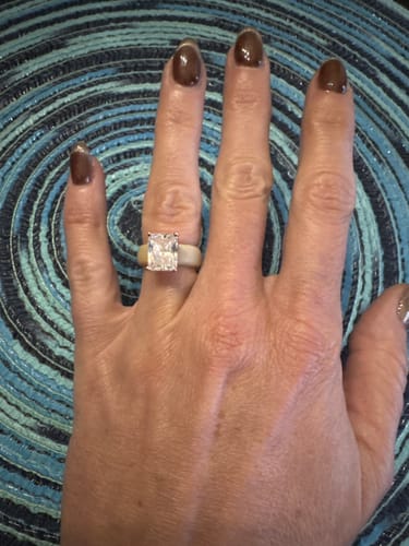 Reviewer's hand wearing the Silicone Ring with a large, emerald-cut CZ stone against a patterned blue background.