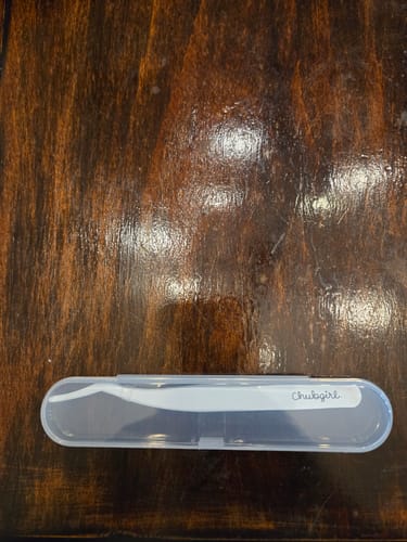 Customer's white Sticker Tweezer in its semi-transparent plastic case, lying on a wooden surface.