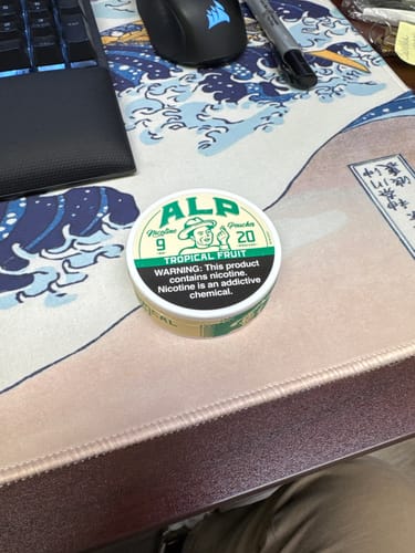 A reviewer's round tin of ALP Tropical Fruit Nicotine Pouches sitting on a desk.