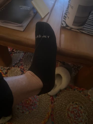 Customer showing the fit of the black Ankle Sock on their foot indoors.