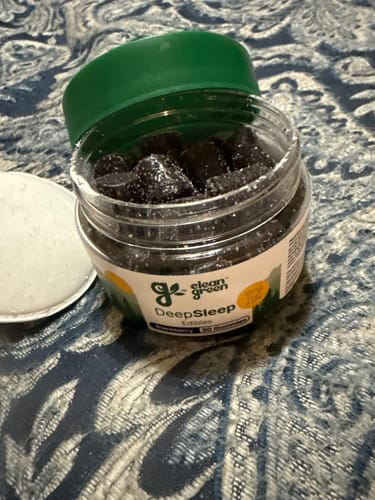 Customer's open jar of dark, sugar-coated DeepSleep Gummies on a patterned surface.