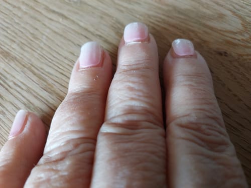 Hand einer Kundin mit den 'Babyboomer Pink' UV Gelnägeln, die nach einer Woche Tragezeit einen leichten Ansatz zeigen.