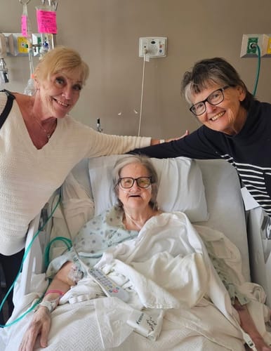 Customer's photo of two people smiling next to a loved one in a hospital bed.