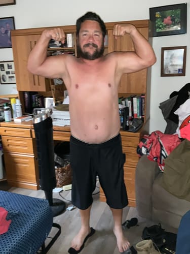 Reviewer flexing shirtless to show his physique before a gym workout for his Liquid L-Carnitine review.