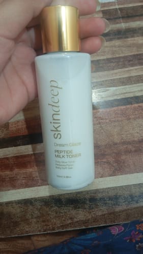 Customer holding a white bottle of Skindeep Peptide Milk Toner with a gold cap.