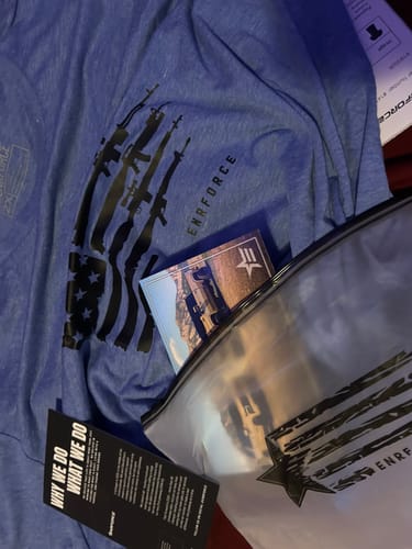 Customer's blue Ladies Armed Patriot Tee with a rifle-flag graphic, laid out with its packaging.
