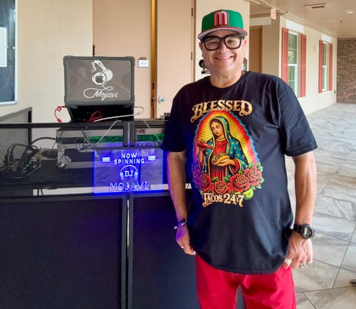 Reviewer wearing the black 'Blessed - Tacos 24:7 T-Shirt' while standing next to DJ equipment.