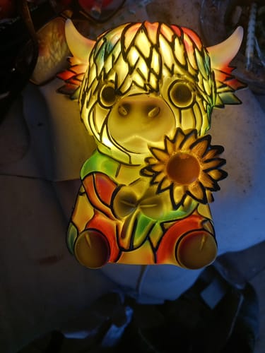 Customer's colorful Highland Cow LED Night Light figurine glowing in a dark setting, holding a sunflower.