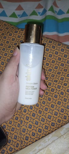 Customer holding the white bottle of DREAM GLAZE Peptide Milk Toner with a shiny gold cap.