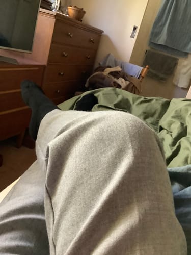 Customer relaxing on a bed, wearing the comfortable black Crew Socks with grey pants.
