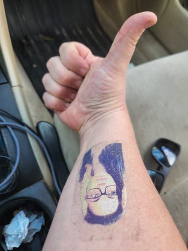 Reviewer gives a thumbs-up, showing a Custom Photo Face Temporary Tattoo of a woman on their forearm.