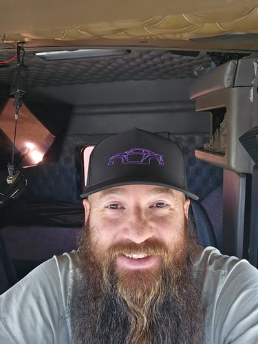 Customer smiling while wearing the black 80Eighty DCG88 Hat with a purple car logo inside a vehicle.