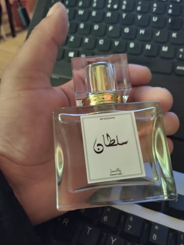 Customer holding a square, glass perfume bottle with a white label in their hand.
