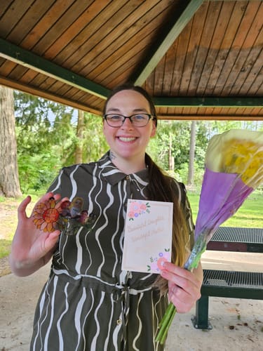 Customer smiling while holding her personalized Sunflower Mom and Kids Sitting suncatcher with a card and flowers.