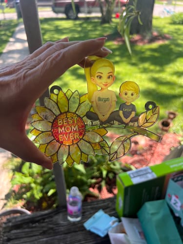 Close-up of a hand holding the personalized sunflower suncatcher with a mom and two children.