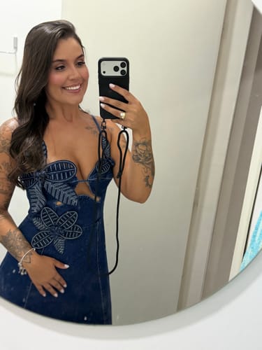 Cliente tirando uma selfie no espelho, mostrando a case preta com alça de pescoço para celular.
