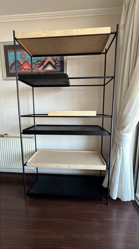 Cliente muestra la estantería LUXE armada en su casa, con estructura negra y bandejas de madera y negras.