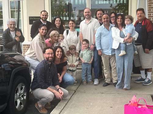 Reviewer wearing the blue Dara Denim Tube Jumpsuit with a white jacket, standing with a large group of people outdoors.