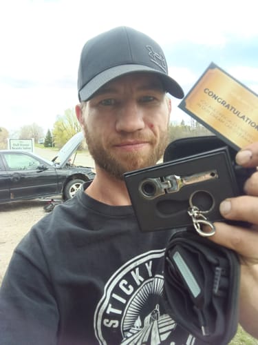 Customer holding the 10mm Wrench Keychain in its open case with a car in the background.