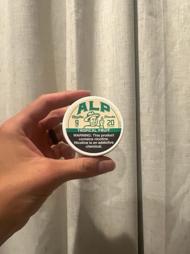 Reviewer holding the round, white can of ALP Tropical Fruit Nicotine Pouches.