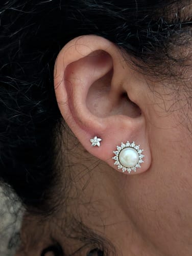 Customer wearing the petite Silver Flower Bloom Earrings on their ear next to another stud.