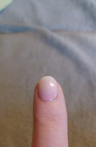Nahaufnahme des Fingers einer Kundin mit einem kurzen, runden Nagel, der mit dem UV-Gel Babyboomer Pink manikürt ist.