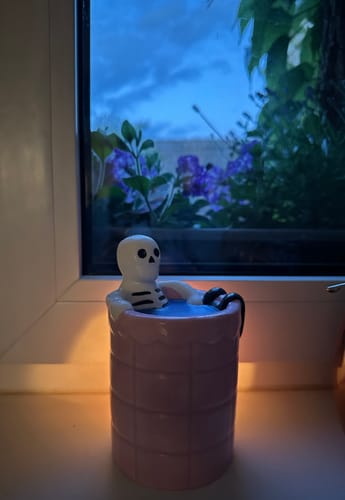 Rezensentin zeigt die beleuchtete Duftlampe „Dead Cool“ auf einer Fensterbank. Das Skelett im Pool sorgt für eine gemütliche Atmosphäre.