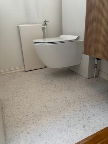 Anmelder viser det ferdige resultatet av Lisboa Terrazzo hvit selvklebende fliser lagt på et badegulv.