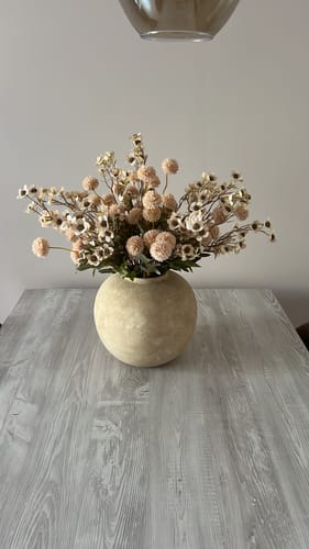 Recensent toont het crèmekleurige Wax Arrangement in een bijpassende ronde vaas op een grijze tafel.
