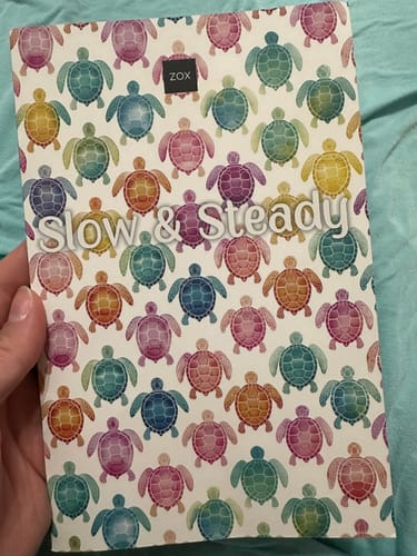 A customer holds the May 2026 Booklet featuring a colorful turtle pattern and the words 'Slow & Steady' on the cover.