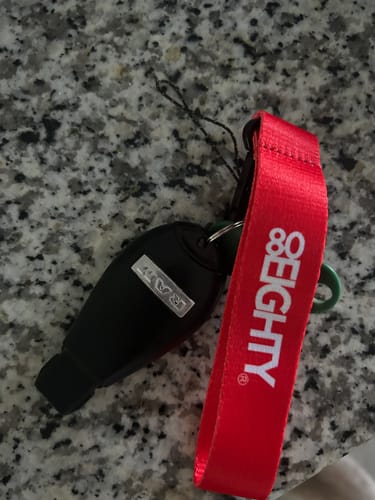 Customer's red 80Eighty WristStrap keychain attached to a black car key fob on a granite countertop.