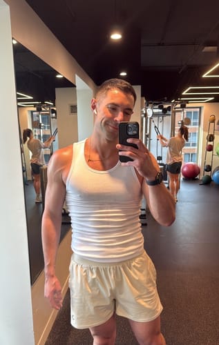 Reviewer taking a mirror selfie in the gym wearing a white, fitted Premium Ultra-Soft Cotton Tank.