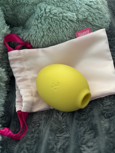 Customer's yellow Lem Clitoral Massager on a fluffy teal blanket next to its white storage pouch.
