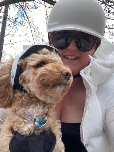 Close-up of a reviewer and their dog, both wearing helmets, riding in the Kvisp Dog Bike Carrier.